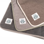 Three neutral-toned pet throw blankets with a branded label on them, displayed in an overlapped fashion.