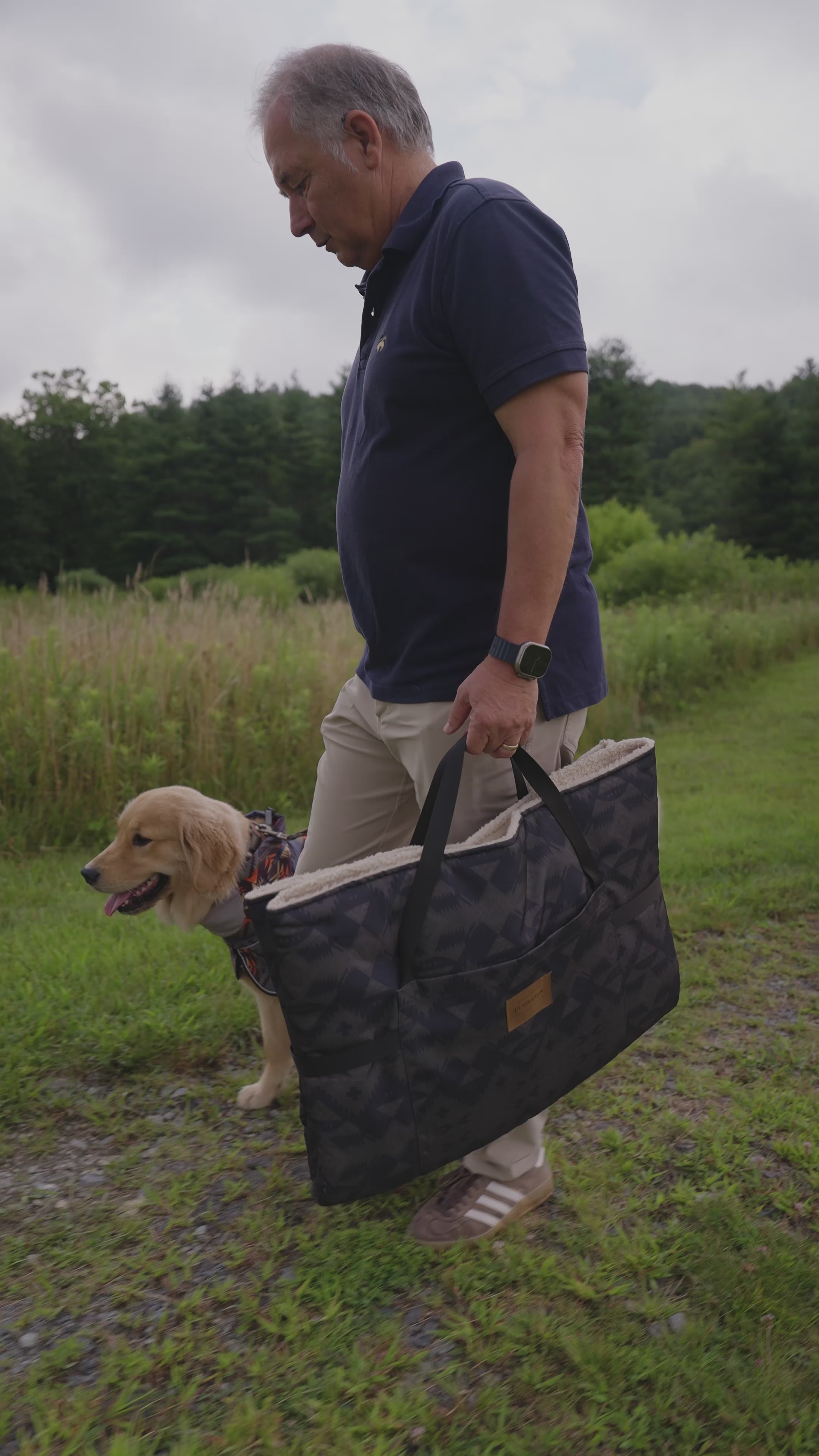 Load video: Man and dog walking in the grass until the man lays down a Pendleton travel dog bed for the dog.